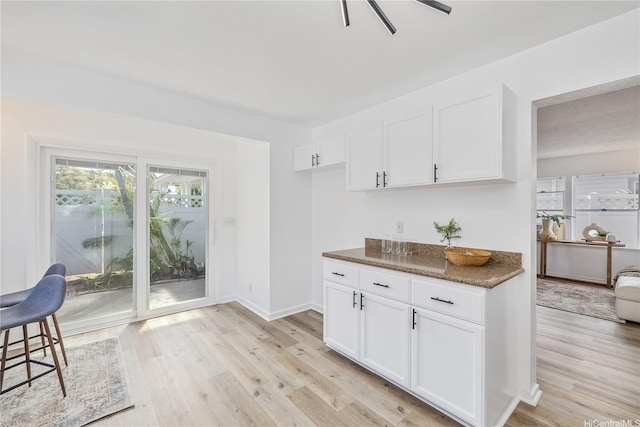 kitchen featuring dark stone counters, white cabinets, baseboards, and light wood-style floors