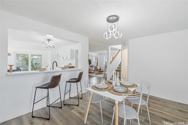 dining area with a notable chandelier, sink, light wood-type flooring, and a textured ceiling