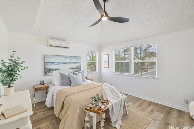 bedroom with an AC wall unit, ceiling fan, light hardwood / wood-style floors, and a textured ceiling