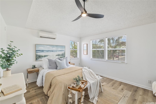 bedroom featuring wood finished floors, a textured ceiling, a ceiling fan, and a wall unit AC