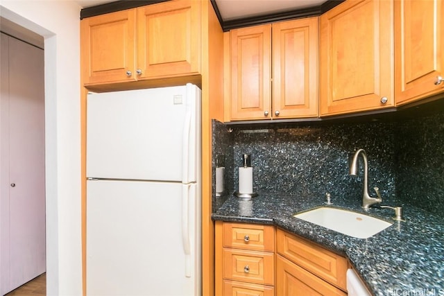 kitchen featuring sink, decorative backsplash, dark stone counters, and white fridge