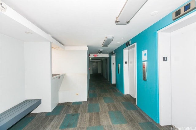 hallway with elevator and dark colored carpet