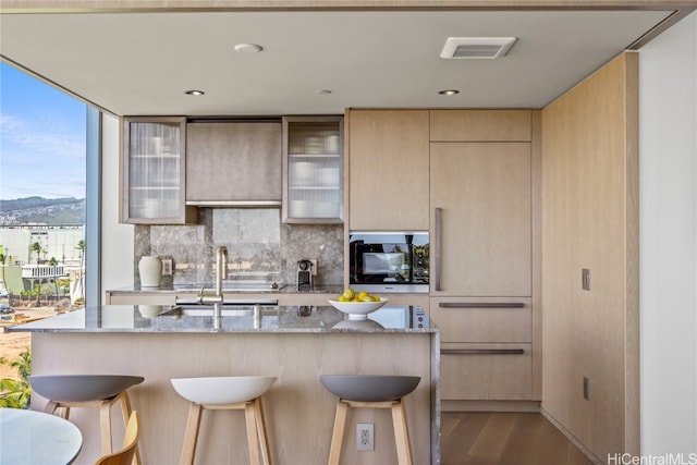 kitchen with a kitchen breakfast bar, a kitchen island with sink, light stone counters, and light wood-type flooring