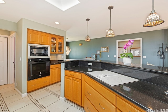 kitchen with a skylight, hanging light fixtures, light tile patterned floors, and black appliances