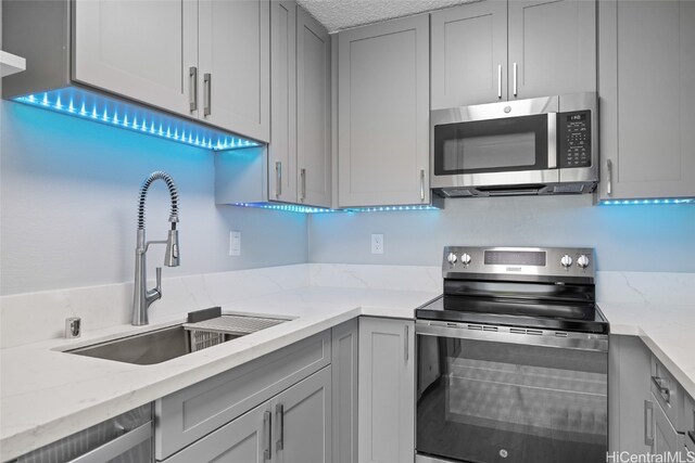 kitchen featuring appliances with stainless steel finishes, light stone countertops, sink, and gray cabinetry