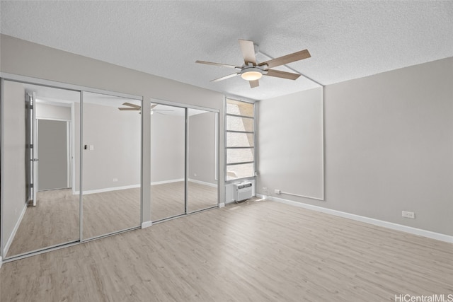 unfurnished bedroom featuring ceiling fan, multiple closets, a textured ceiling, and light hardwood / wood-style flooring