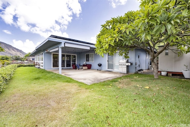 rear view of property featuring a mountain view, a patio, and a lawn