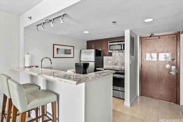 kitchen featuring decorative backsplash, kitchen peninsula, stainless steel appliances, a breakfast bar, and light stone counters