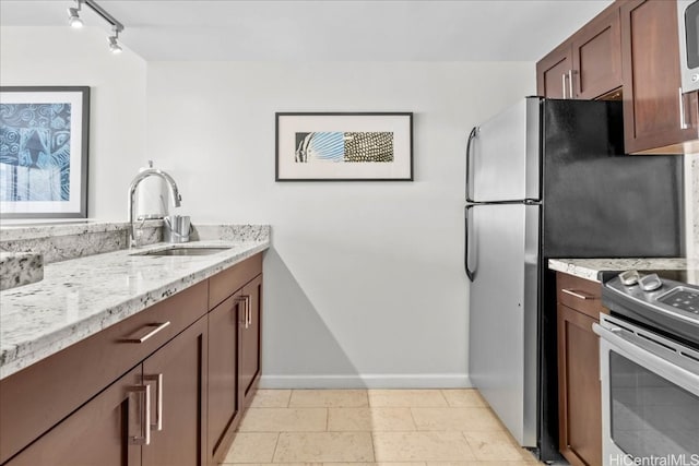 kitchen featuring rail lighting, light stone counters, stainless steel appliances, and sink