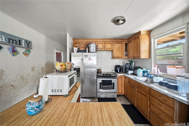 kitchen featuring light hardwood / wood-style flooring, wood walls, appliances with stainless steel finishes, and sink