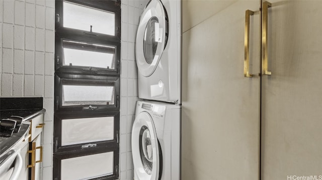 washroom featuring stacked washing maching and dryer and tile walls