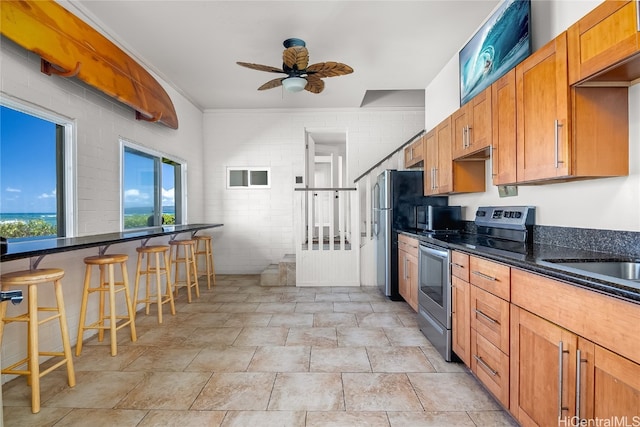 kitchen with dark stone counters, brick wall, a breakfast bar, appliances with stainless steel finishes, and ceiling fan