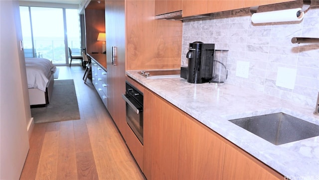 kitchen featuring oven, electric stovetop, backsplash, light stone counters, and light hardwood / wood-style floors