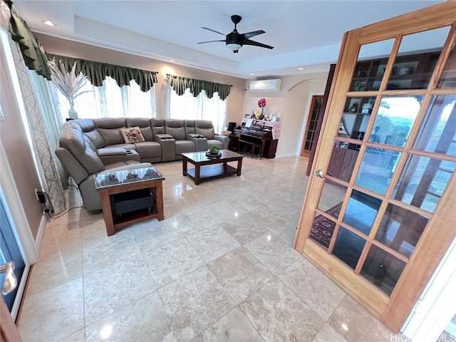 living room featuring a wall mounted air conditioner, a tray ceiling, and ceiling fan