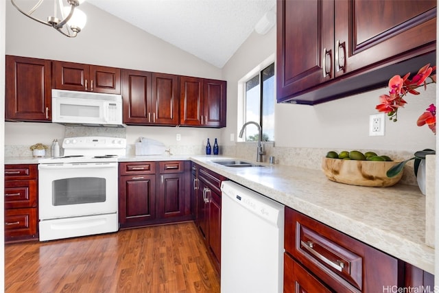 kitchen with vaulted ceiling, dark hardwood / wood-style floors, sink, white appliances, and an inviting chandelier