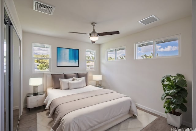 bedroom with a closet, multiple windows, wood-type flooring, and ceiling fan