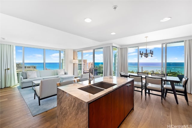 kitchen with a center island with sink, sink, pendant lighting, a water view, and light hardwood / wood-style floors