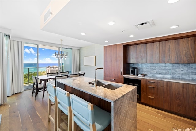 kitchen featuring a center island with sink, light wood-type flooring, sink, decorative light fixtures, and a water view