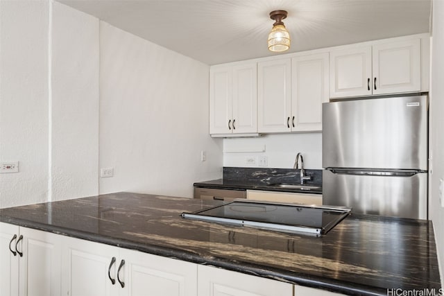 kitchen with stainless steel fridge, white cabinetry, dark stone countertops, and sink