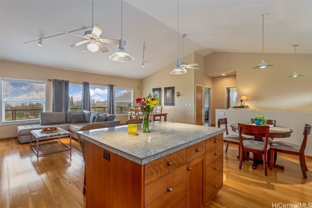 kitchen with a ceiling fan, vaulted ceiling, light wood-style floors, open floor plan, and hanging light fixtures