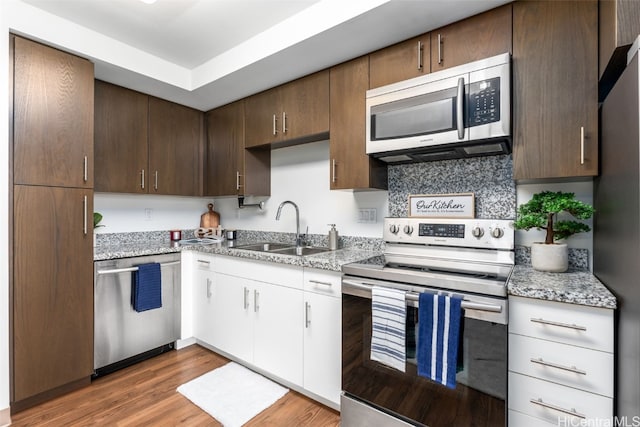 kitchen featuring dark hardwood / wood-style flooring, appliances with stainless steel finishes, white cabinetry, light stone countertops, and sink