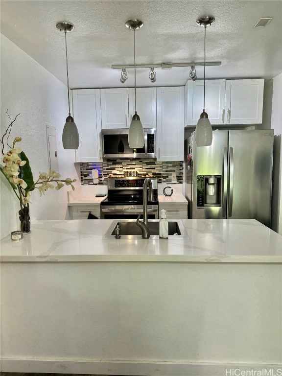 kitchen with tasteful backsplash, appliances with stainless steel finishes, sink, pendant lighting, and white cabinets