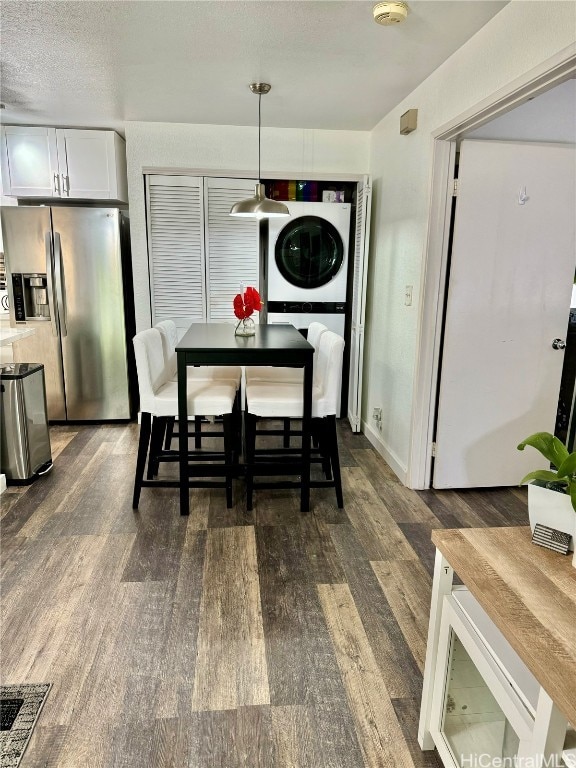 dining space with a textured ceiling, stacked washer / drying machine, and dark hardwood / wood-style flooring