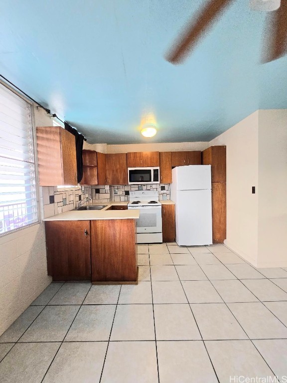 kitchen featuring white appliances, light tile patterned flooring, sink, backsplash, and kitchen peninsula