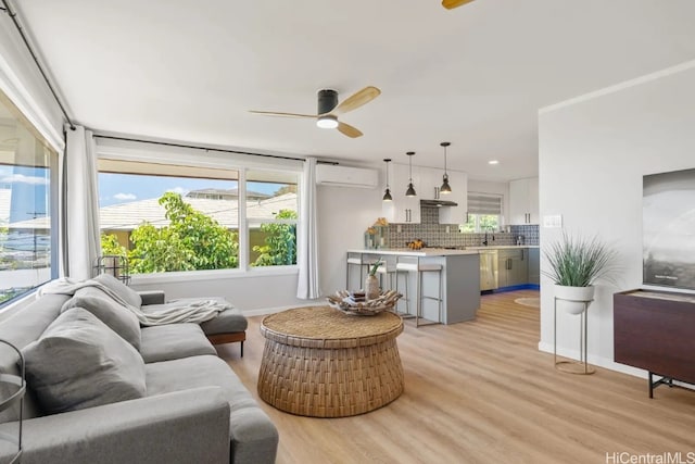 living room with light hardwood / wood-style flooring, a wall mounted AC, sink, and ceiling fan