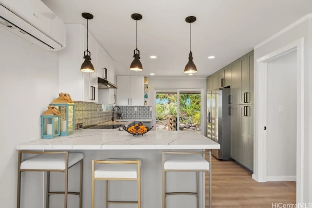 kitchen with a wall unit AC, kitchen peninsula, a kitchen bar, light hardwood / wood-style floors, and sink