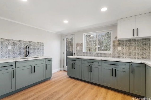 kitchen featuring decorative backsplash, white cabinetry, light wood-type flooring, ornamental molding, and sink