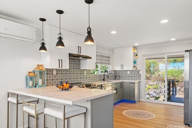 kitchen featuring kitchen peninsula, white cabinets, an AC wall unit, and hanging light fixtures