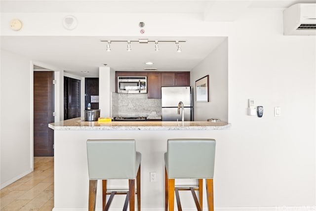 kitchen featuring kitchen peninsula, appliances with stainless steel finishes, backsplash, a kitchen breakfast bar, and a wall mounted AC