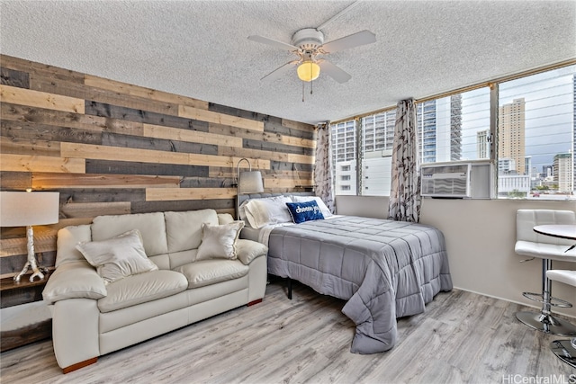 bedroom featuring a textured ceiling, wooden walls, light wood-type flooring, and ceiling fan