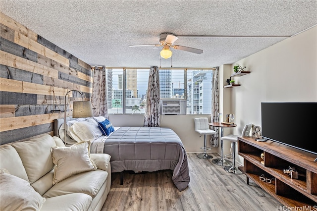 bedroom with hardwood / wood-style floors, ceiling fan, expansive windows, cooling unit, and a textured ceiling