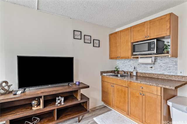 kitchen with sink, a textured ceiling, decorative backsplash, and light hardwood / wood-style flooring