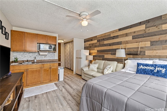 bedroom with wood walls, a textured ceiling, light hardwood / wood-style floors, ceiling fan, and white fridge