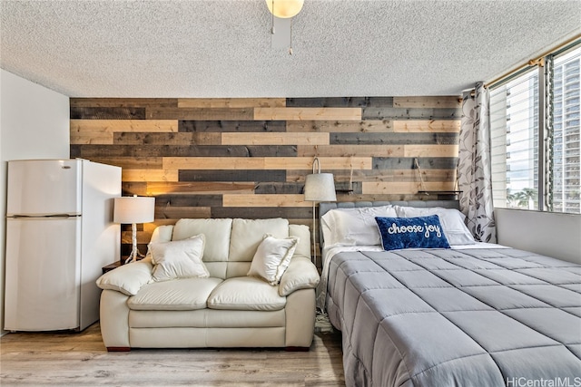 bedroom featuring wood walls, light hardwood / wood-style flooring, a textured ceiling, and white refrigerator