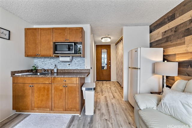 kitchen with wooden walls, backsplash, sink, light wood-type flooring, and white refrigerator