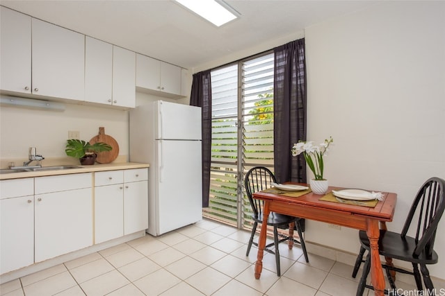 kitchen with white cabinetry, sink, light tile patterned floors, and white refrigerator