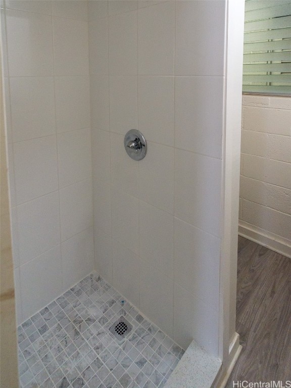 bathroom with a tile shower and wood-type flooring