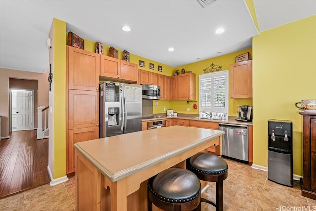 kitchen featuring a kitchen breakfast bar, light wood-type flooring, stainless steel appliances, sink, and a center island