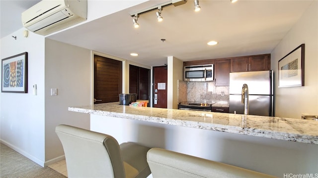 kitchen featuring kitchen peninsula, a wall mounted AC, a kitchen bar, stainless steel appliances, and light stone counters