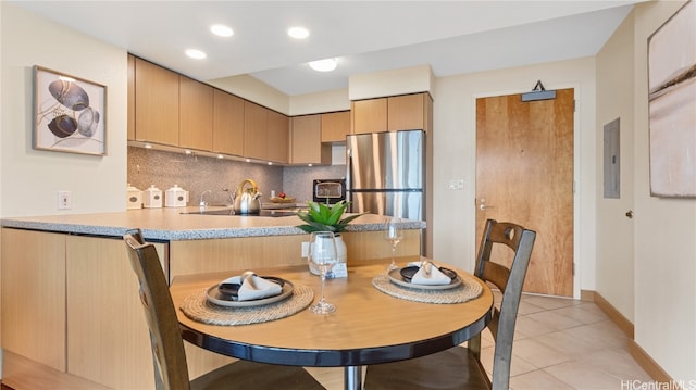 kitchen with backsplash, electric panel, stainless steel refrigerator, light tile patterned floors, and light brown cabinets