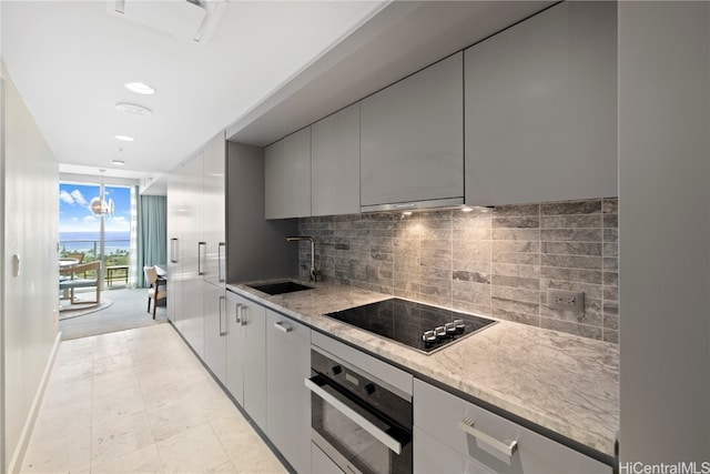 kitchen featuring decorative backsplash, sink, stainless steel oven, and light stone counters