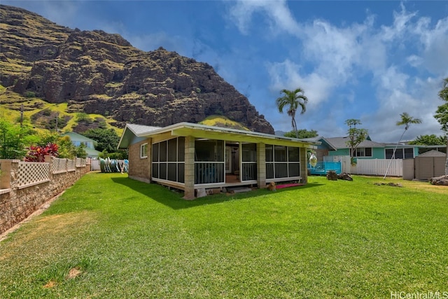 rear view of house featuring a sunroom, a storage unit, a mountain view, and a lawn