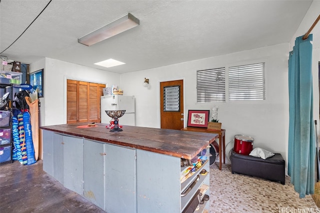 kitchen featuring butcher block countertops, a textured ceiling, white refrigerator, and concrete flooring