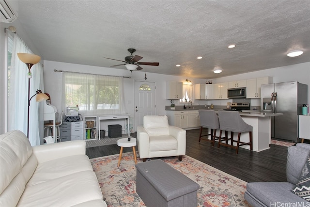 living room featuring a wall unit AC, ceiling fan, a textured ceiling, dark wood-type flooring, and sink