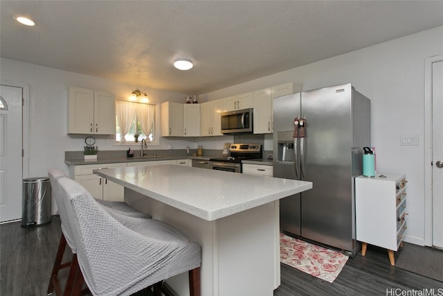 kitchen with appliances with stainless steel finishes, white cabinetry, dark hardwood / wood-style floors, sink, and a center island