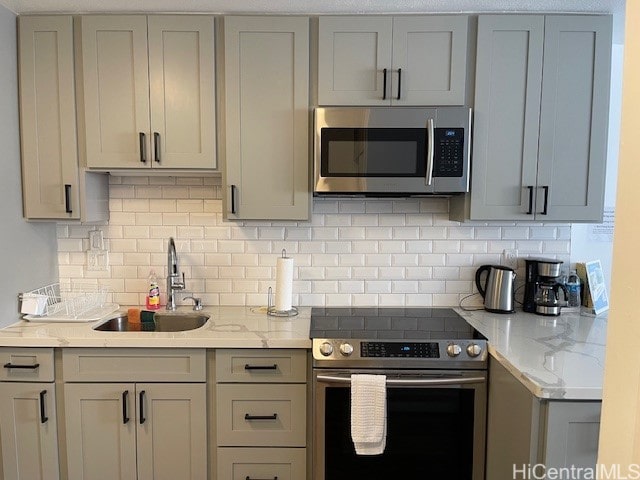 kitchen featuring appliances with stainless steel finishes, decorative backsplash, sink, and light stone counters